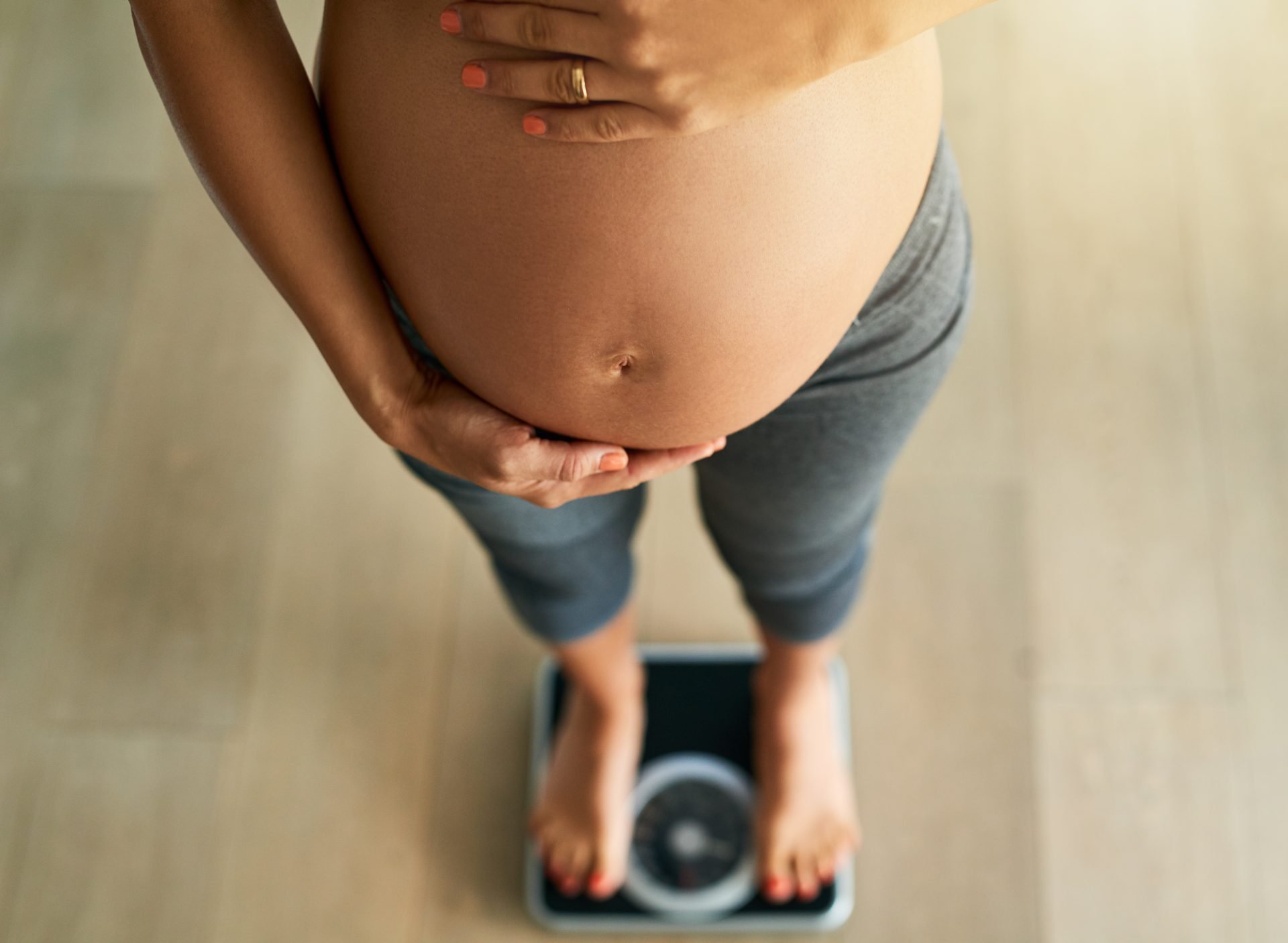 pregnancy by the pounds. cropped high angle shot of a pregnant woman weighing herself on a scale.