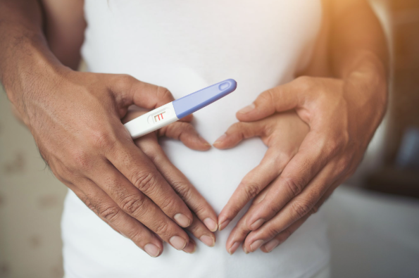 Casal segurando teste de gravidez sobre barriga, representando fertilidade e planejamento reprodutivo