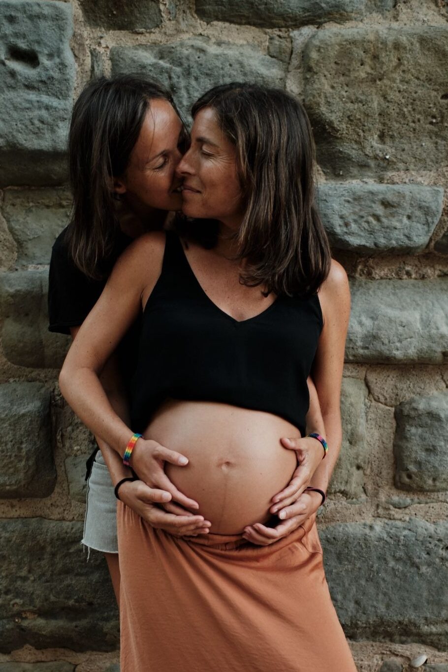 Casal homoafetivo feminino celebra a gravidez após tratamento de reprodução assistida, com gestante sendo abraçada pela parceira.