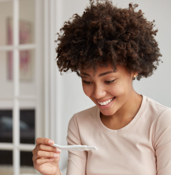 Mulher sorrindo enquanto observa um teste de gravidez, representando planejamento reprodutivo, fertilidade e decisões relacionadas à maternidade.
